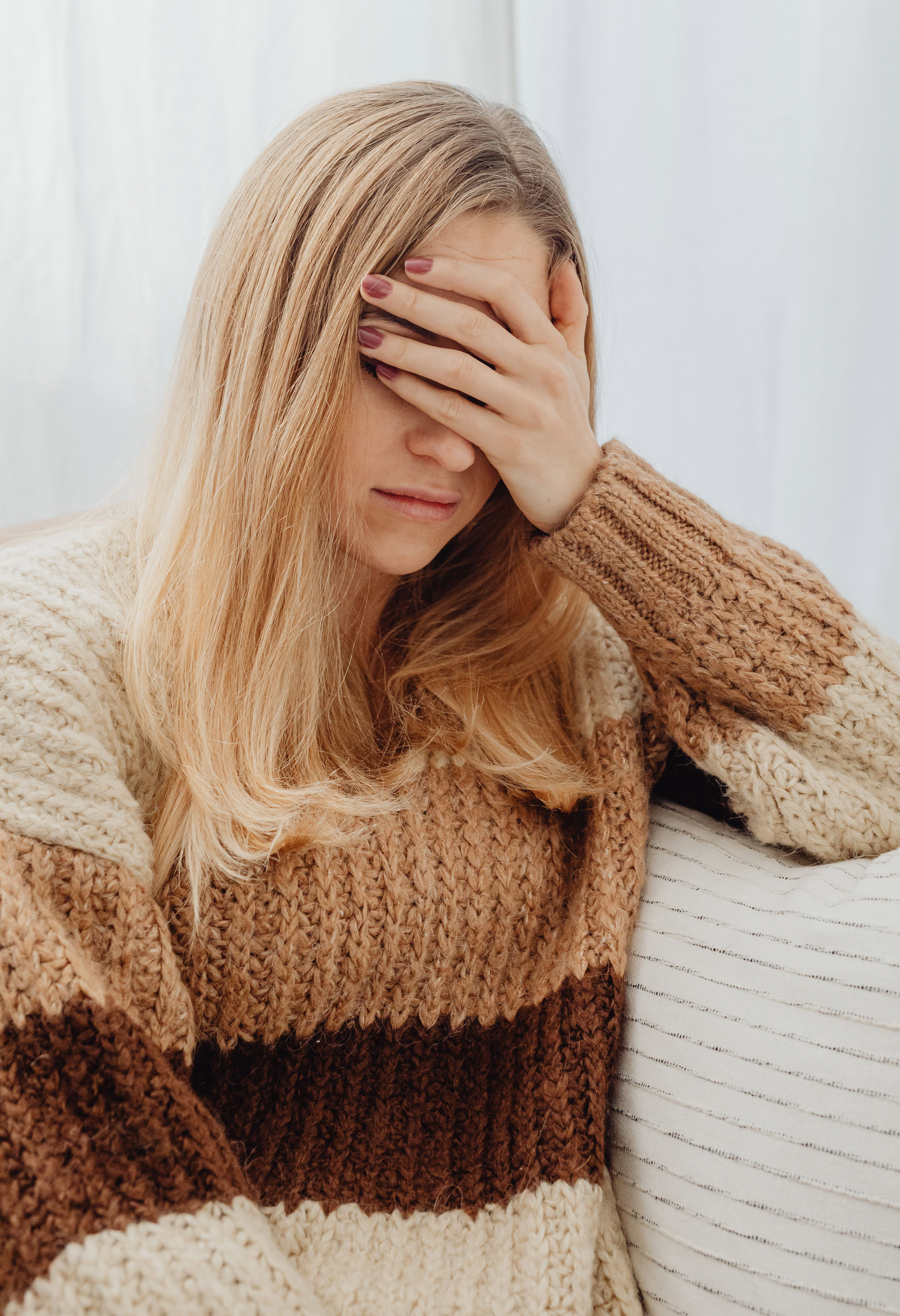 woman covering face with hands while sitting in a chair