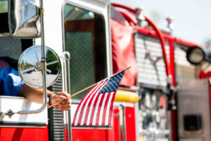 firetruck with a fireman holding an american flag out of the window