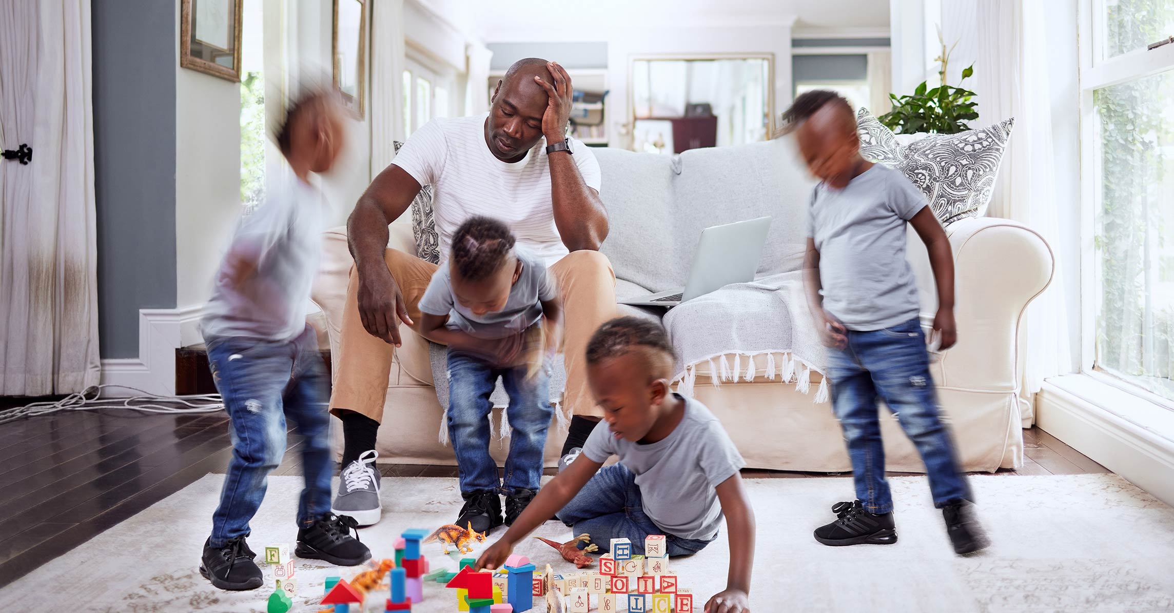 male holding his head while his children run around